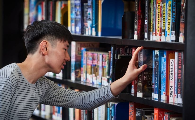 Teenager looking at books on library shelf