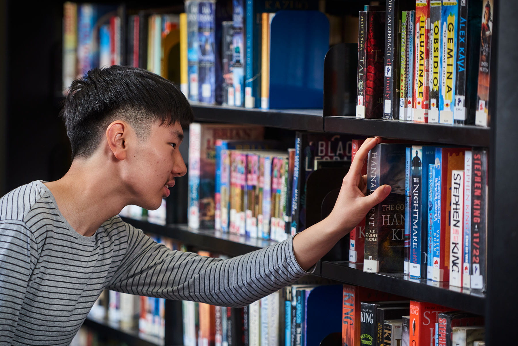 Teenager looking at books on library shelf