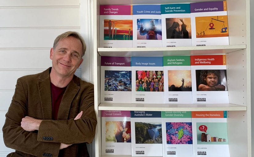 Justin Healey stands next to a display of past editions of Issues in Society