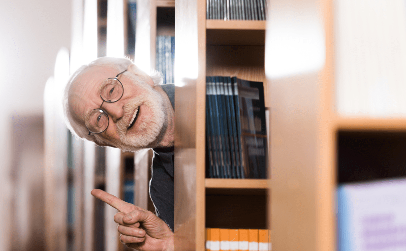 Librarian leaning out from behind shelves whilst making a gesture that indicates he has an idea, he looks happy